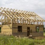 New cottage of natural ecological lumber materials under construction in green field. Wooden walls and steep roof frame. Property, investment, professional building and reconstruction concept.
